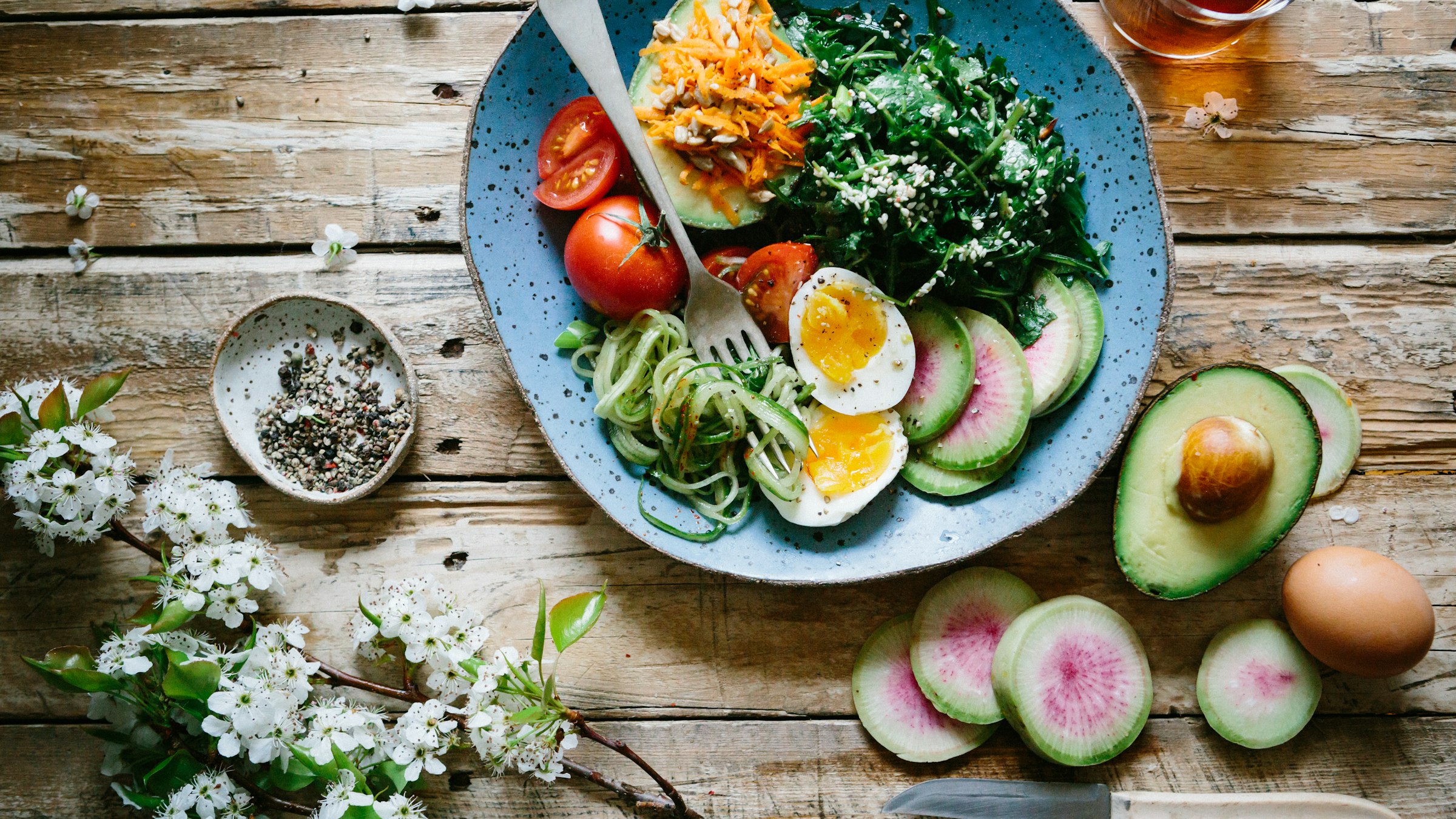 Overhead flat-lay of a fresh salad bowl with sliced vegetables and an avocado on a rustic wooden table